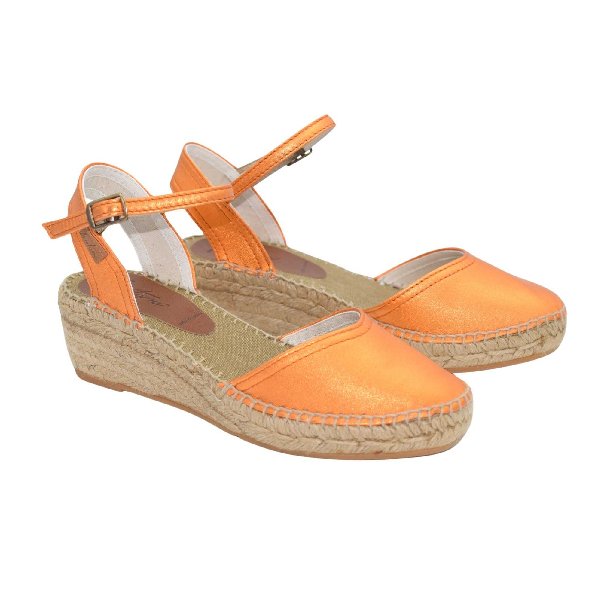Alpargata de cuña baja en piel metalizada naranja. Empeine cerrado y talonera abierta. Cuenta con un tirante de la misma piel metalizada con una hebilla corredera para un ajuste perfecto. Cuña de yute 100% orgánico con base antideslizante. Alpargata cosida a mano con hilo de algodón 100%.